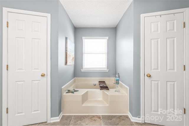 full bath featuring a garden tub, a textured ceiling, and baseboards