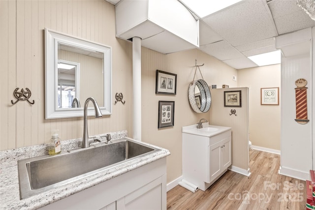 full bath featuring two vanities, a sink, a drop ceiling, and wood finished floors