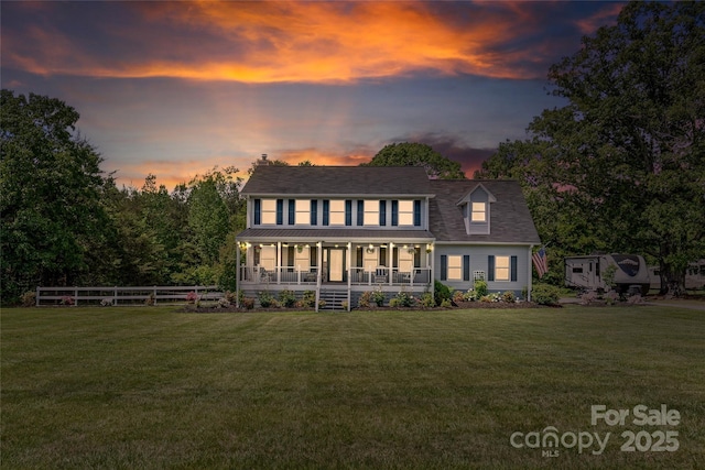 view of front facade featuring covered porch, fence, and a lawn