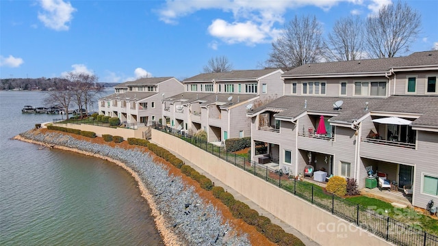 rear view of property with a water view, a residential view, fence, and roof with shingles