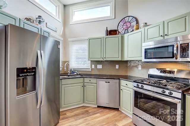 kitchen featuring stainless steel appliances, a sink, backsplash, light wood finished floors, and dark countertops