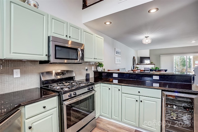 kitchen with beverage cooler, a peninsula, light wood-style floors, appliances with stainless steel finishes, and backsplash