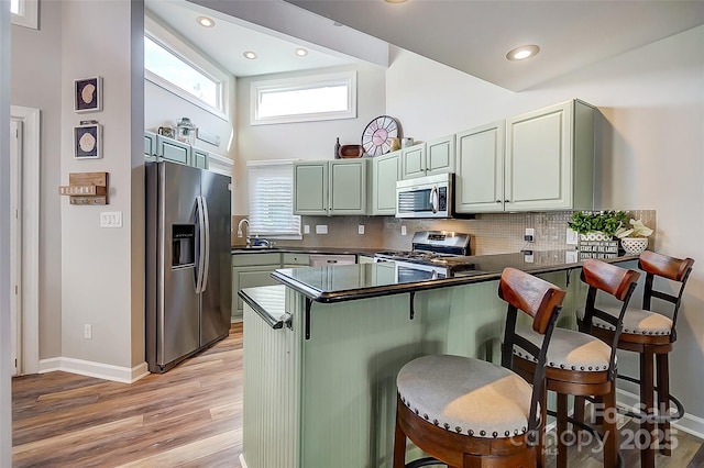 kitchen featuring tasteful backsplash, dark countertops, light wood-style flooring, a peninsula, and stainless steel appliances