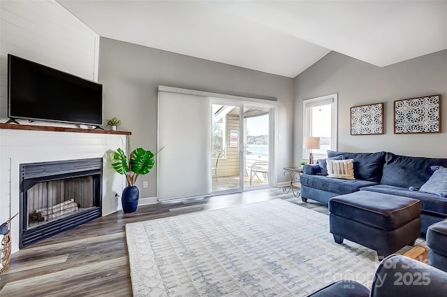 living room featuring lofted ceiling, a fireplace, baseboards, and wood finished floors