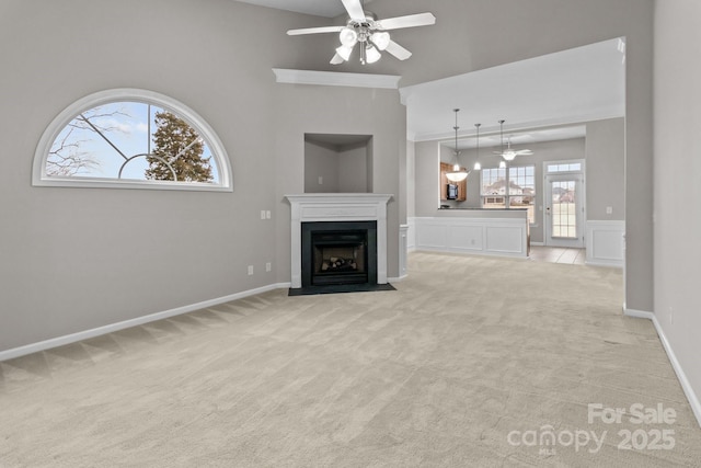 unfurnished living room with ceiling fan, ornamental molding, and light carpet