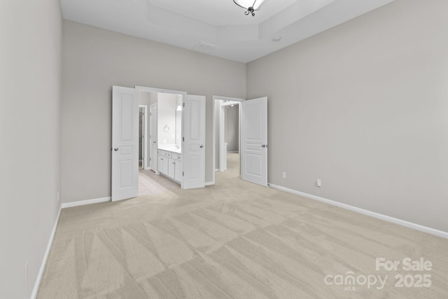 unfurnished bedroom with light carpet, a raised ceiling, and ensuite bathroom