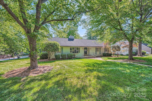 ranch-style home featuring a chimney, a shingled roof, and a front yard