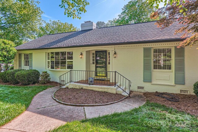 single story home with roof with shingles, a chimney, a front yard, and brick siding