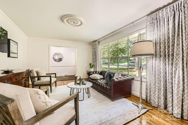 living room featuring baseboards, ornamental molding, wood finished floors, and visible vents