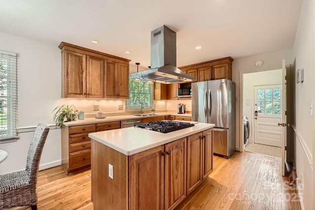 kitchen with island exhaust hood, a sink, light countertops, stainless steel appliances, and light wood-style flooring