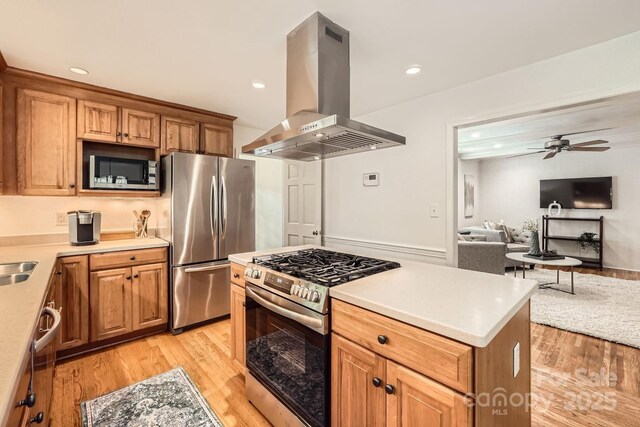 kitchen featuring open floor plan, light wood-type flooring, island exhaust hood, a ceiling fan, and appliances with stainless steel finishes