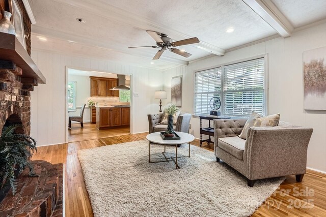 living area with light wood-type flooring, ceiling fan, a wealth of natural light, and beamed ceiling