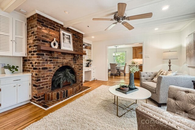 living room featuring a ceiling fan, a fireplace, light wood-type flooring, beam ceiling, and ornamental molding