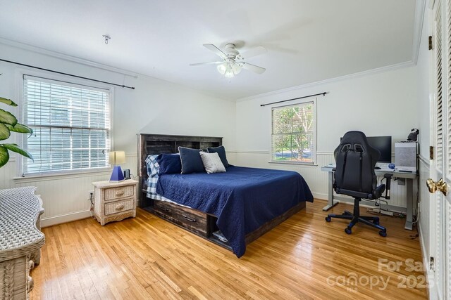 bedroom with light wood-style floors, ceiling fan, wainscoting, and crown molding