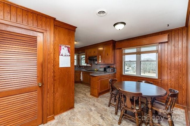 kitchen with brown cabinets, stainless steel counters, visible vents, wooden walls, and under cabinet range hood