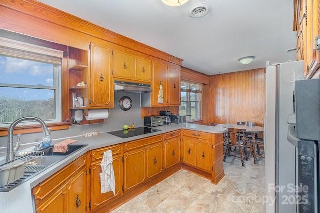 kitchen featuring black electric stovetop, under cabinet range hood, a sink, light countertops, and brown cabinets