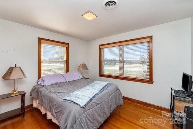 bedroom with baseboards, multiple windows, visible vents, and wood finished floors