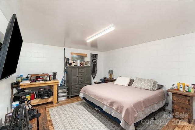 bedroom featuring concrete block wall and wood finished floors