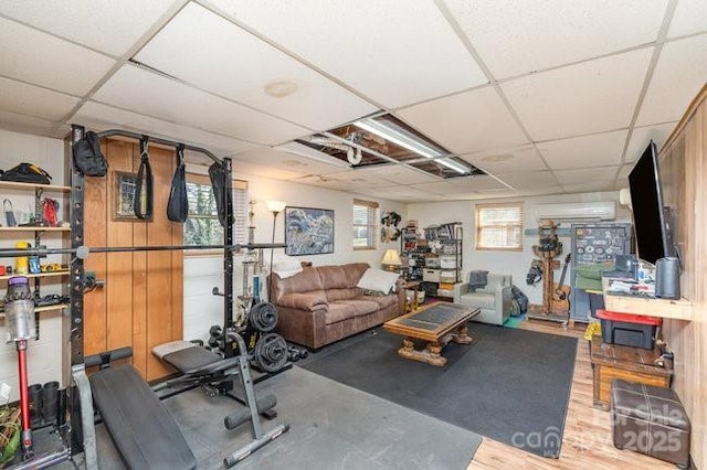 workout room with a paneled ceiling, an AC wall unit, and wood finished floors