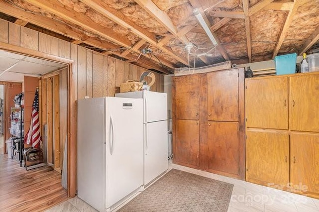 unfinished below grade area featuring wooden walls and freestanding refrigerator