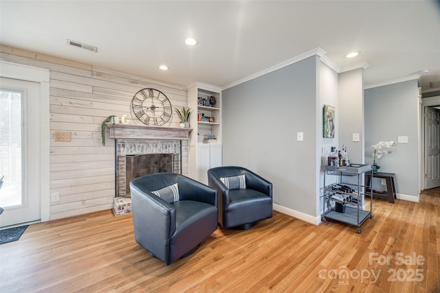 living room featuring crown molding, wooden walls, a fireplace, and light hardwood / wood-style flooring