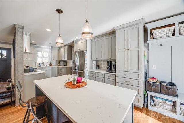 kitchen with hanging light fixtures, stainless steel fridge, gray cabinets, a kitchen island, and backsplash