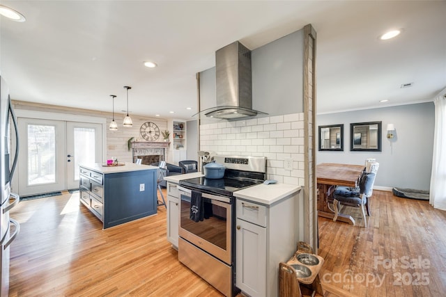 kitchen featuring pendant lighting, wall chimney range hood, a kitchen island, stainless steel electric stove, and light wood-type flooring