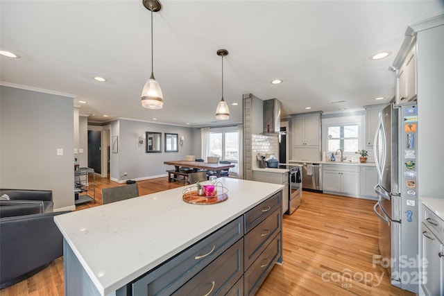 kitchen featuring wall chimney exhaust hood, appliances with stainless steel finishes, plenty of natural light, a kitchen island, and pendant lighting