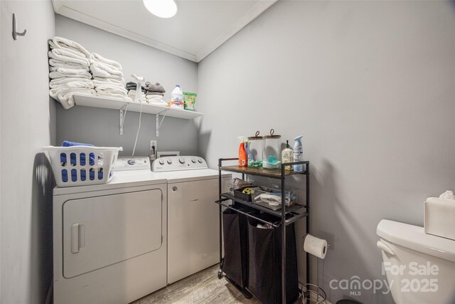 laundry area with light hardwood / wood-style flooring, ornamental molding, and washing machine and clothes dryer