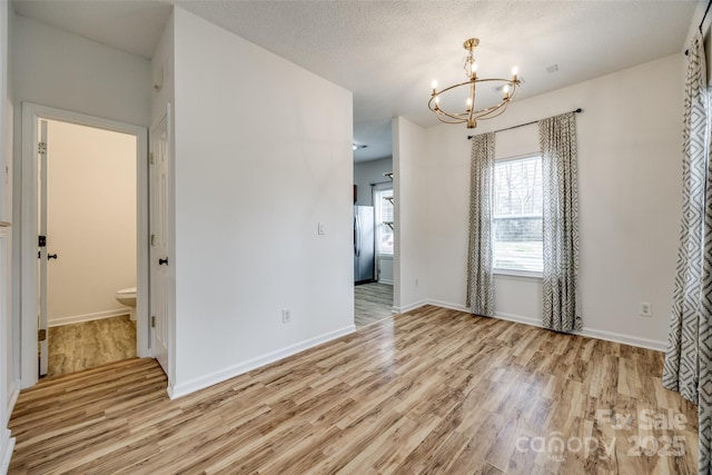 11426 Savannah Creek Dr, Charlotte, NC 28273 - empty room featuring light wood-style floors, baseboards, a textured ceiling, and an inviting chandelier