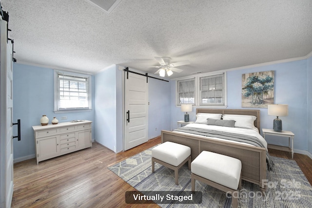 bedroom with a barn door, light wood-type flooring, a textured ceiling, ceiling fan, and crown molding