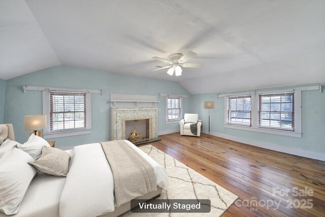 bedroom with wood-type flooring, lofted ceiling, a high end fireplace, and ceiling fan