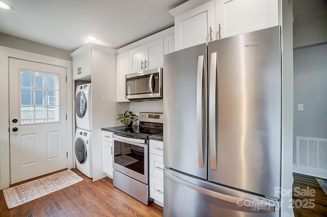 kitchen with appliances with stainless steel finishes, stacked washer and clothes dryer, white cabinets, and light hardwood / wood-style floors