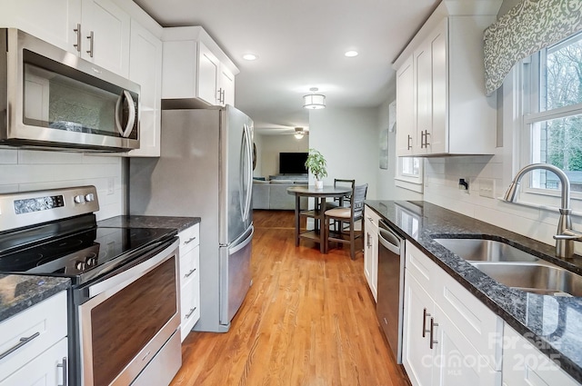 kitchen with sink, light hardwood / wood-style flooring, appliances with stainless steel finishes, white cabinetry, and dark stone counters