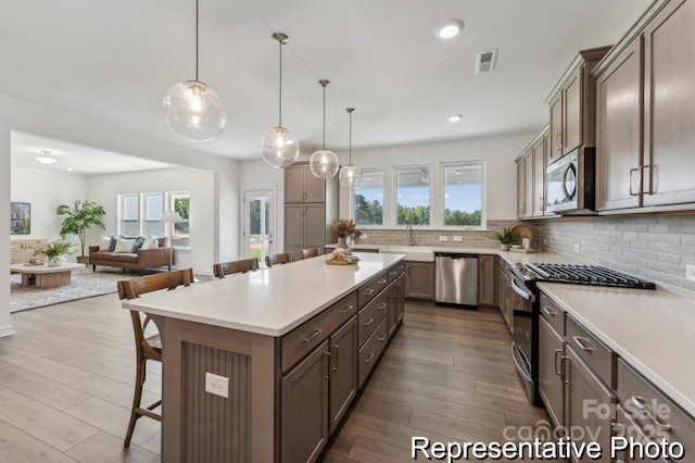 kitchen with appliances with stainless steel finishes, decorative light fixtures, tasteful backsplash, a kitchen breakfast bar, and a center island