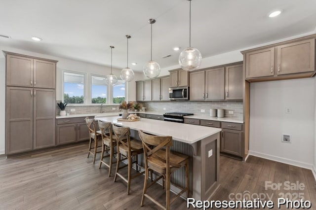 kitchen featuring a kitchen island, a breakfast bar, pendant lighting, dark hardwood / wood-style floors, and stainless steel appliances