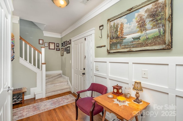 entryway featuring a decorative wall, a wainscoted wall, wood finished floors, stairway, and crown molding