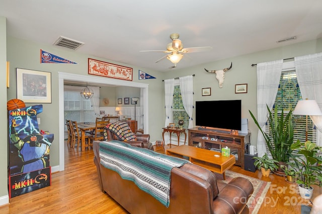 living area featuring light wood-style flooring, visible vents, and ceiling fan with notable chandelier