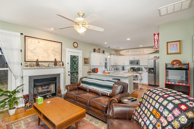 living area with light wood finished floors, visible vents, ceiling fan, a fireplace, and recessed lighting