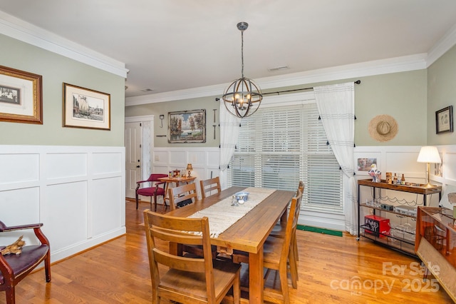 dining area with light wood-style floors, visible vents, ornamental molding, and an inviting chandelier