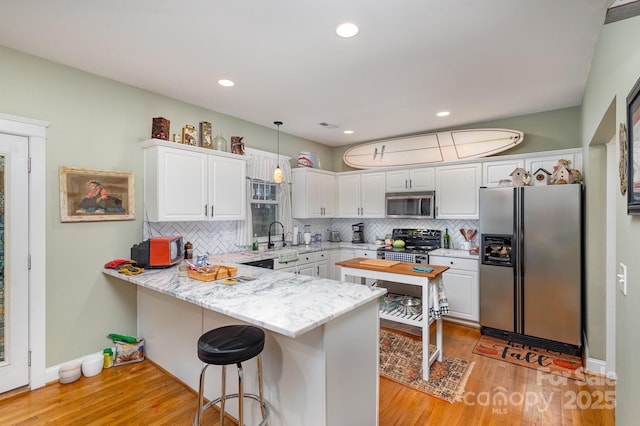 kitchen featuring stainless steel appliances, white cabinetry, a peninsula, and decorative light fixtures