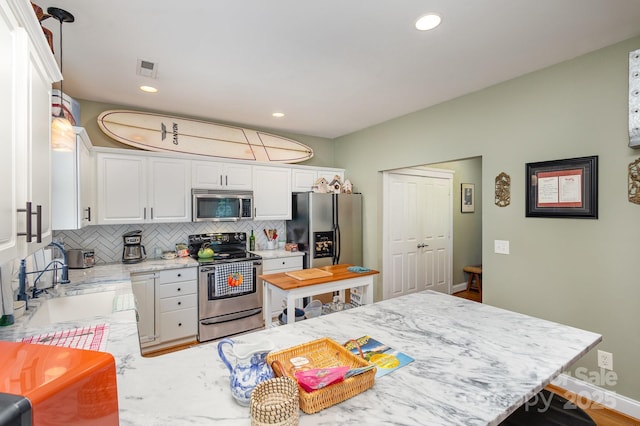 kitchen featuring appliances with stainless steel finishes, white cabinets, backsplash, and pendant lighting