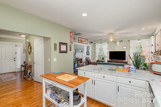 kitchen featuring light wood-style floors, a ceiling fan, open floor plan, white cabinetry, and light stone countertops