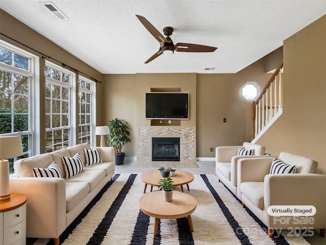 living area with a ceiling fan, a tile fireplace, visible vents, and a textured ceiling