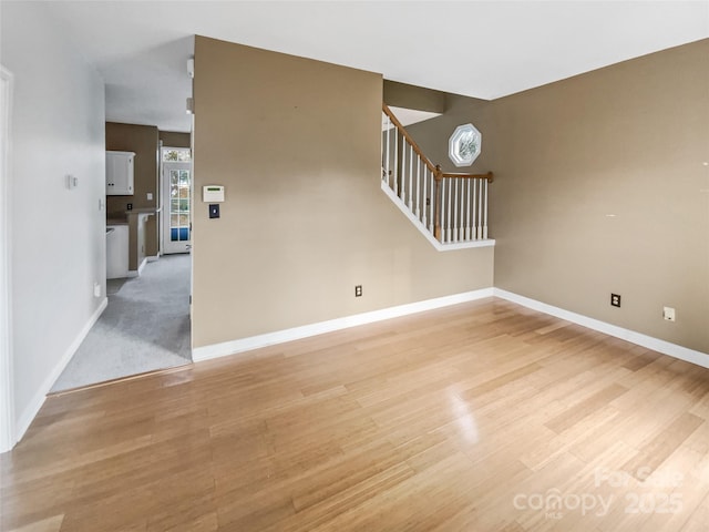 empty room with light wood-type flooring, baseboards, and stairs