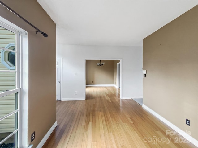 hall with baseboards, a notable chandelier, and light wood finished floors