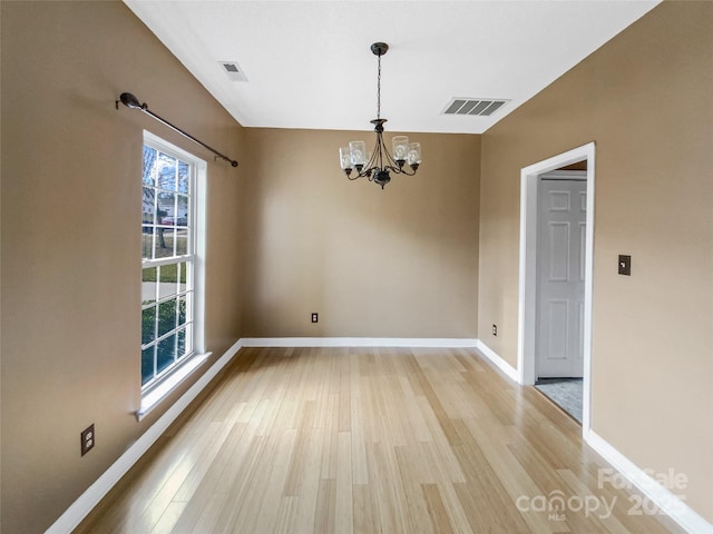 empty room with a chandelier, light wood finished floors, visible vents, and baseboards