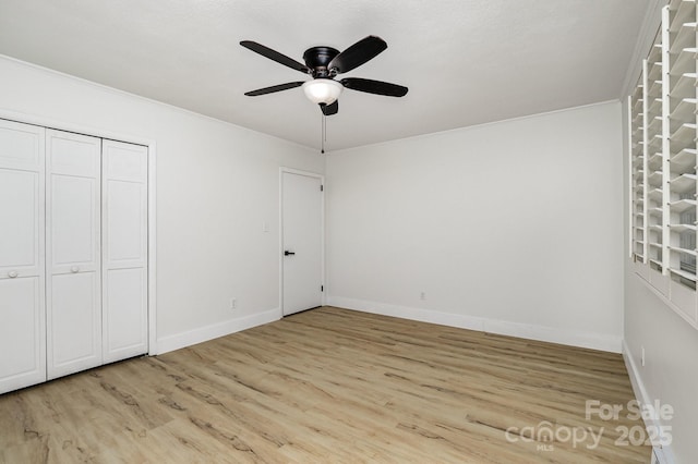 unfurnished bedroom with a closet, baseboards, a ceiling fan, crown molding, and light wood finished floors