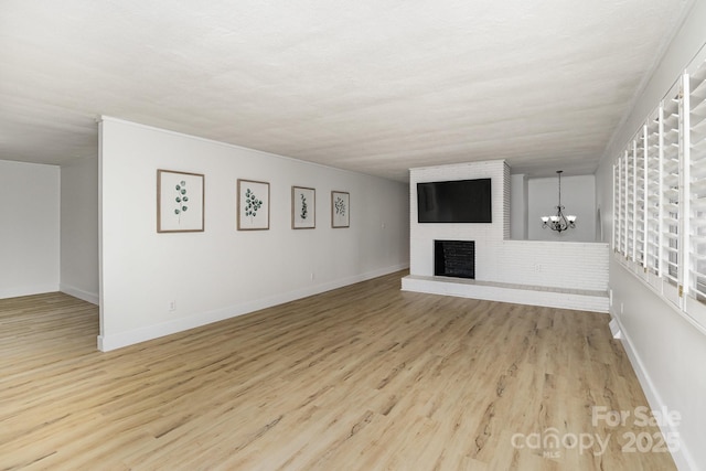 unfurnished living room featuring a chandelier, light wood-type flooring, baseboards, and a brick fireplace