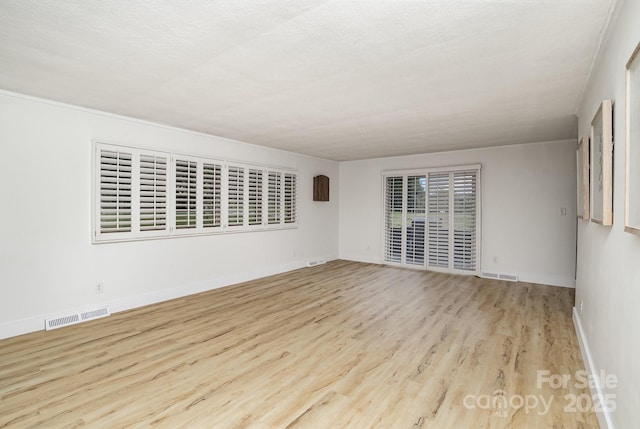 spare room with wood finished floors, baseboards, and visible vents